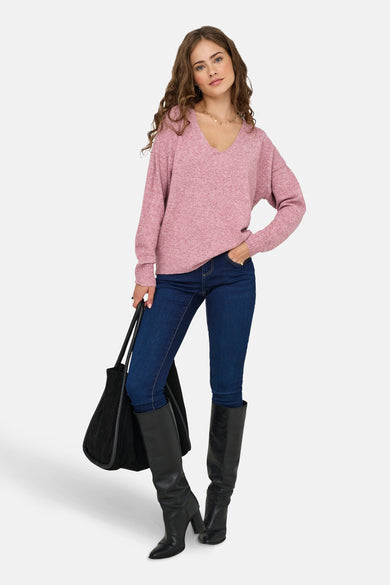 Pull rose à col en V de ONLY, porté avec un jean bleu foncé, des bottes noires et un sac à main.
