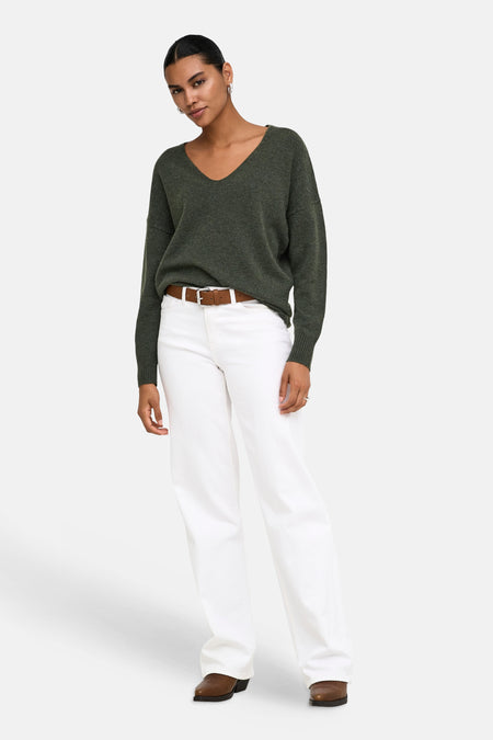 Pull col V vert foncé en maille douce par ONLY®, porté avec un jean blanc et une ceinture marron, vue de face.