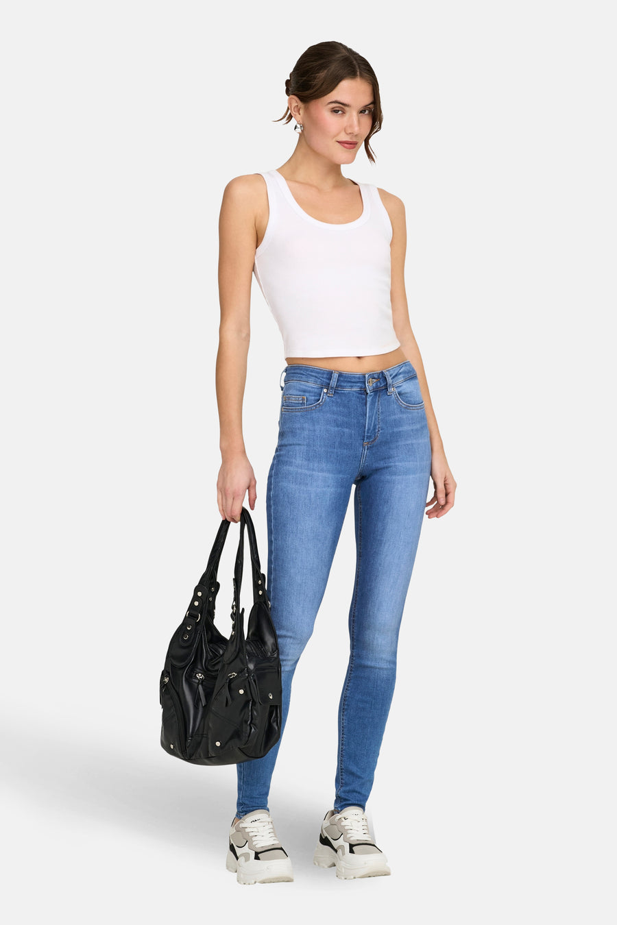 Middelblauwe skinny jeans van ONLY, gedragen met een witte tanktop en een zwarte tas.