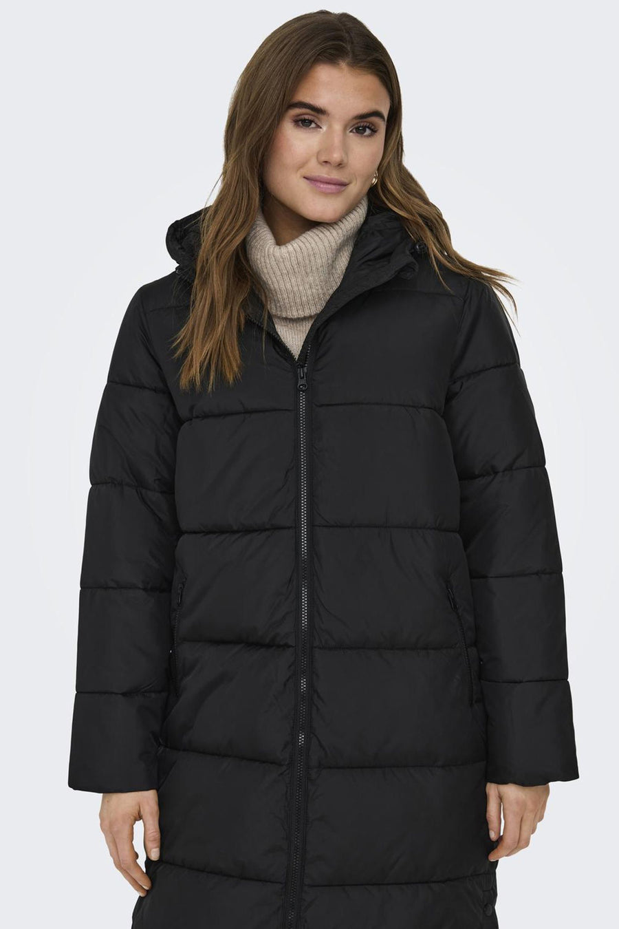 Zwarte lange jas van ONLY®, gewatteerd met ritssluiting, gedragen over een beige coltrui.