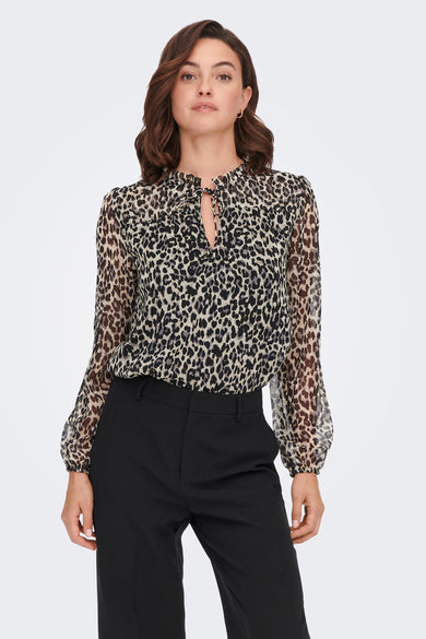Chemisier noir à manches longues de ONLY, avec motif léopard et col à nouer, porté avec un pantalon noir classique.
