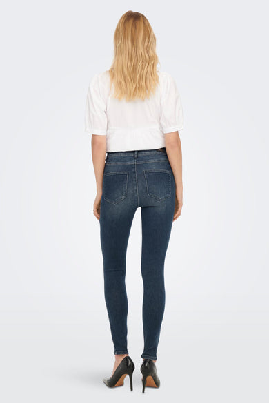 Jean skinny bleu de ONLY, porté avec un chemisier blanc et des escarpins noirs.