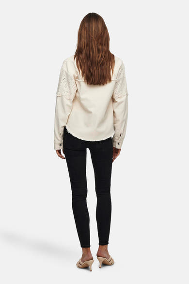 Veste courte écru de ONLY, avec manches longues ajourées et ourlet effiloché, portée avec un jean noir et des mules.
