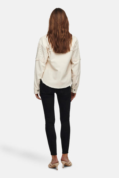 Veste courte écru de ONLY, avec manches longues ajourées et ourlet effiloché, portée avec un jean noir et des mules.
