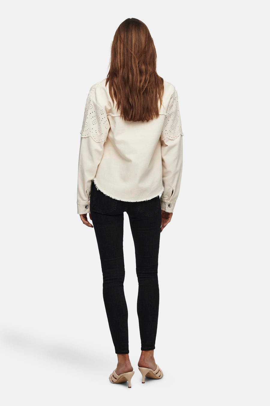 Veste courte écru de ONLY, avec manches longues ajourées et ourlet effiloché, portée avec un jean noir et des mules.

