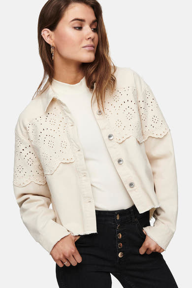 Veste courte écrue de ONLY, ornée de détails ajourés et portée sur un haut blanc uni et un jean noir.
