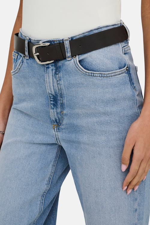 Jean large bleu clair de ONLY, porté avec une ceinture noire classique à boucle argentée.

