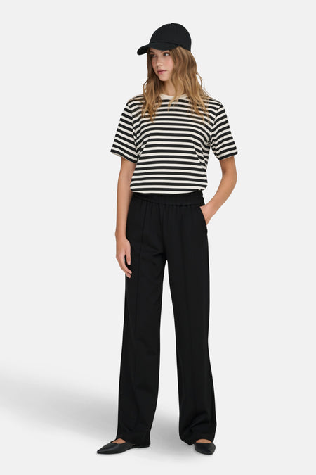 Jogging noir de ONLY, pantalon ample avec une couture sur le devant, porté avec un t-shirt rayé.
