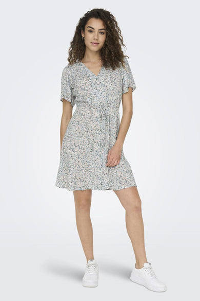 Robe à manches courtes verte de ONLY® avec motif floral, col en V et taille nouée, portée avec des baskets blanches.