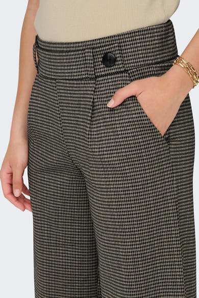 Pantalon gris à carreaux par JDY, avec une main dans la poche et un bracelet doré.
