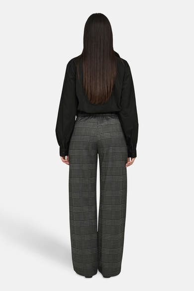 Grijze geruite broek van JDY, wijde pasvorm, gedragen met een zwart overhemd met lange mouwen.