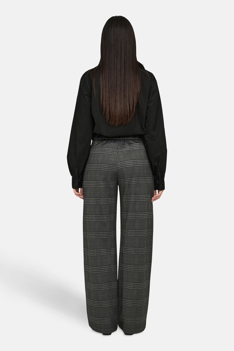 Grijze geruite broek van JDY, wijde pasvorm, gedragen met een zwart overhemd met lange mouwen.