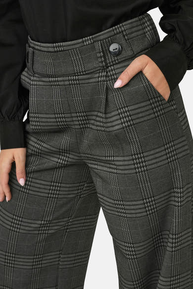Grijze geruite broek van JDY, met een hand in de zak en een zwart overhemd.