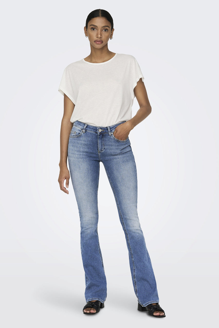 Jean évasé bleu clair de ONLY, porté avec un t-shirt blanc uni et des sandales noires à talons.
