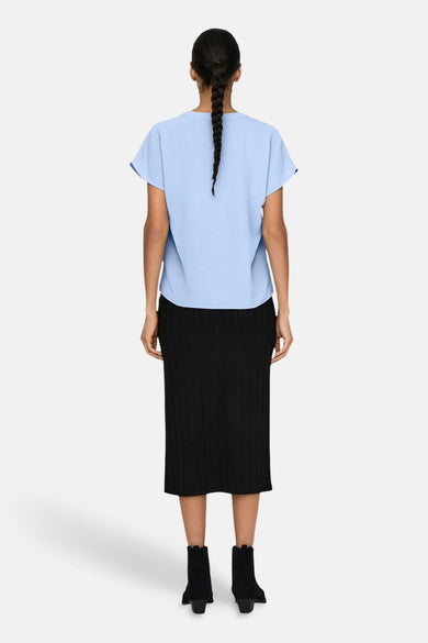Blouse met korte mouwen in het blauw van JDY, met een getextureerde stof, gedragen met een zwarte rok en enkellaarsjes. Achterzicht.