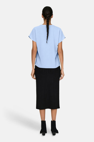 Blouse met korte mouwen in het blauw van JDY, met een getextureerde stof, gedragen met een zwarte rok en enkellaarsjes. Achterzicht.