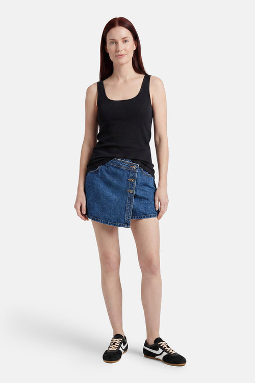 Skort en jean bleu foncé de ONLY avec fermeture boutonnée asymétrique, porté avec un débardeur noir et des baskets.