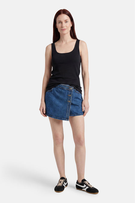 Skort en jean bleu foncé de ONLY avec fermeture boutonnée asymétrique, porté avec un débardeur noir et des baskets.