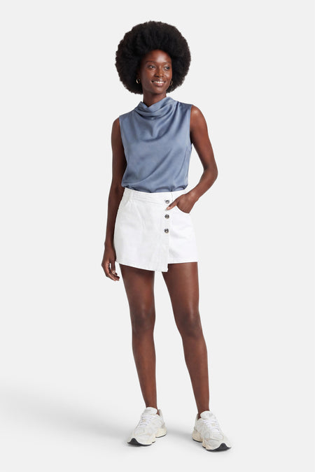 Jupe-short en denim blanc de ONLY®, avec fermeture boutonnée asymétrique, portée avec un top bleu et des baskets.