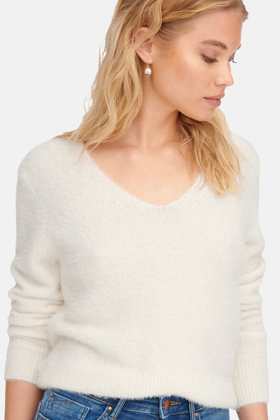 Pull blanc duveteux à col V par ONLY, porté avec un jean en denim brut et des boucles d'oreilles pendantes.