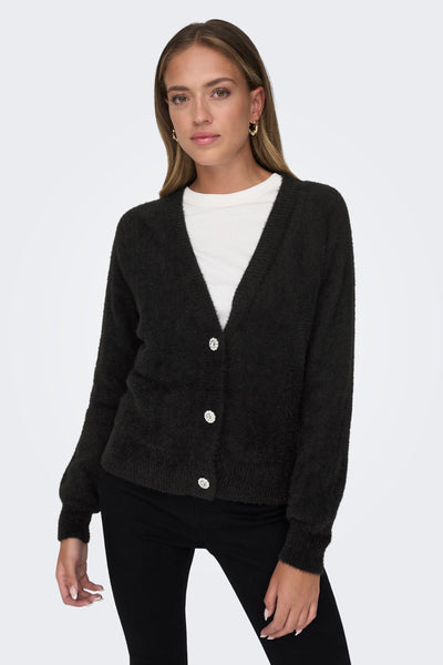 Zwarte pluizige bodywarmer van ONLY, met glanzende decoratieve knopen, gedragen over een wit T-shirt en een zwarte broek.