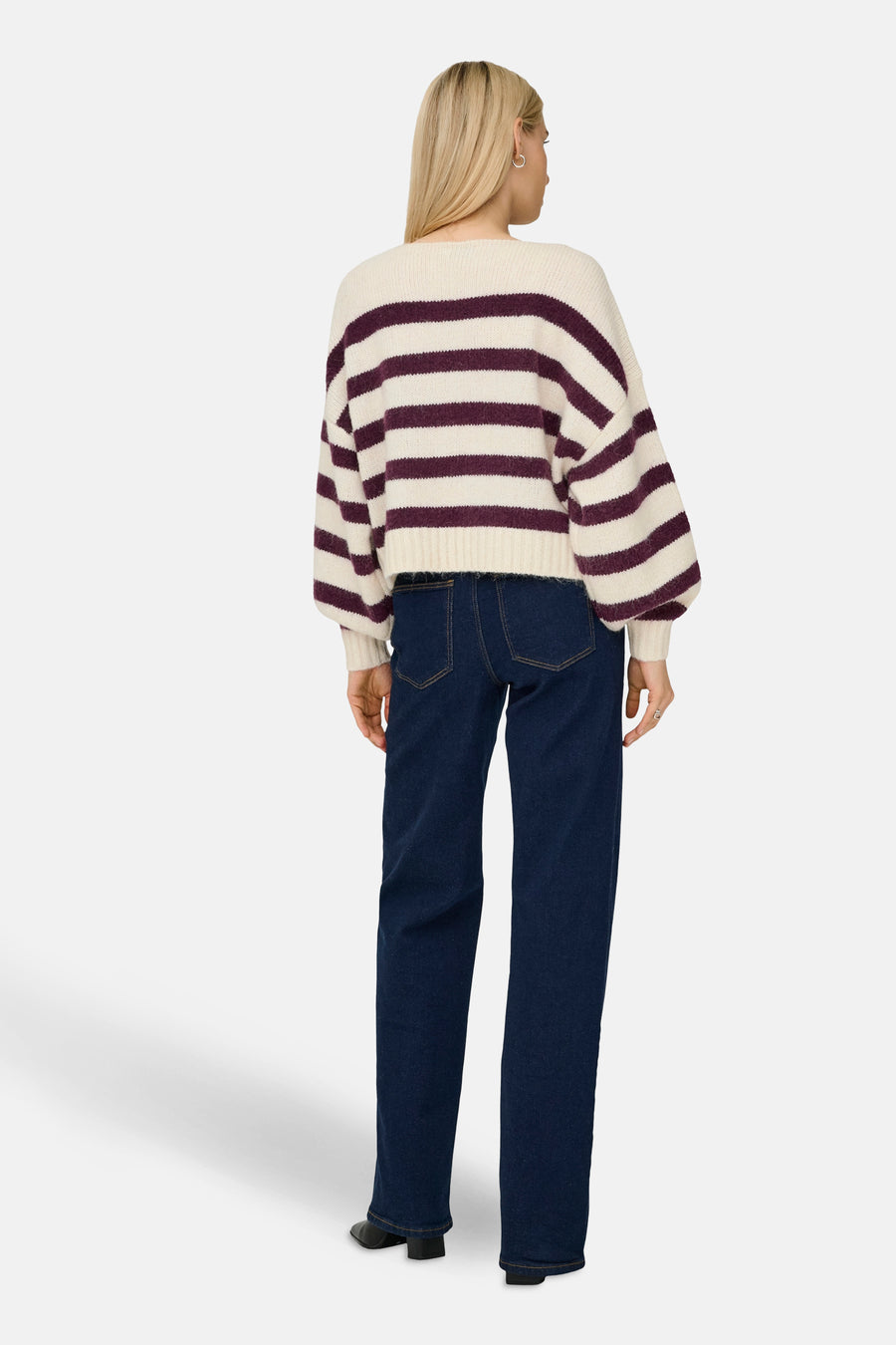 Pull à col rond écru de ONLY® avec des rayures violettes, porté avec un jean bleu foncé et des chaussures noires, vue de dos.