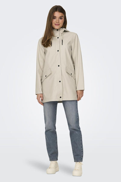 Veste de pluie écru de ONLY, avec capuche, poches à rabat et fermeture à boutons-pression, portée sur un jean et des baskets.

