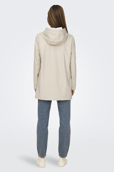 Veste de pluie écrue de ONLY, avec capuche, portée avec un jean bleu et des chaussures crème.