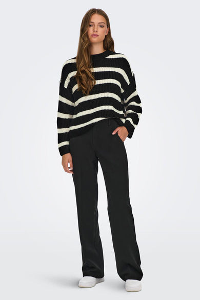 Pull noir de JDY avec des rayures blanches horizontales, porté avec un pantalon noir.
