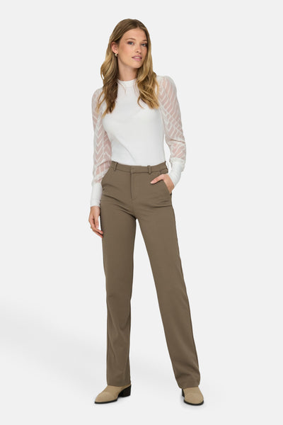 Pantalon brun de ONLY, porté avec un chemisier blanc à manches longues en maille transparente.

