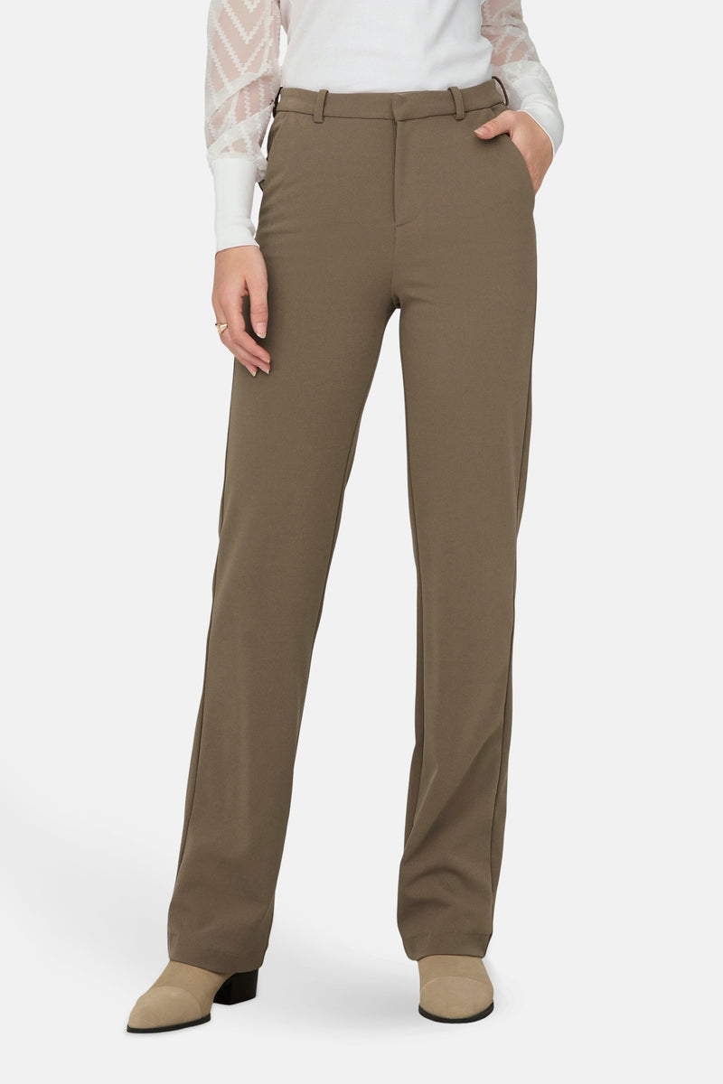 Pantalon marron de ONLY, avec poches, porté avec un chemisier blanc à manches longues transparentes.