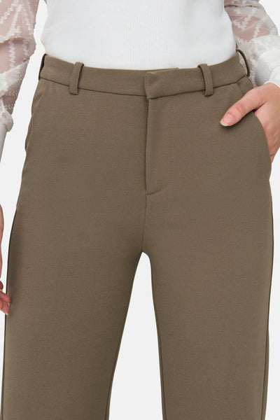 Pantalon marron de ONLY avec passants de ceinture et une main dans la poche, porté avec un haut blanc.
