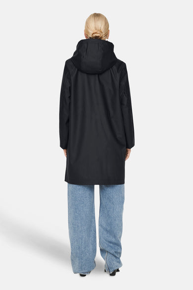 Imperméable noir de ONLY®, avec une capuche, porté avec un jean bleu ample et des talons noirs.