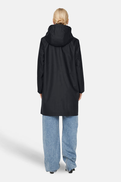 Imperméable noir de ONLY®, avec une capuche, porté avec un jean bleu ample et des talons noirs.