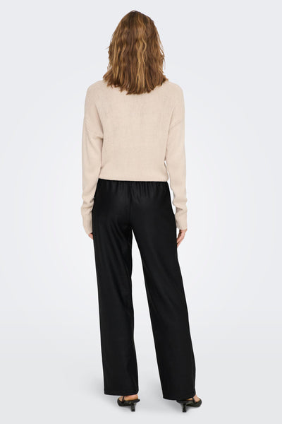 Pantalon noir de ONLY, porté avec un pull beige, avec des chaussures à talons noirs.