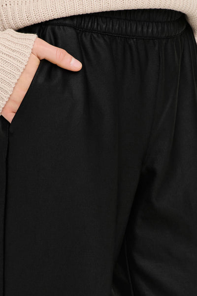 Pantalon noir de ONLY, avec une main dans la poche, porté avec un pull en tricot beige.