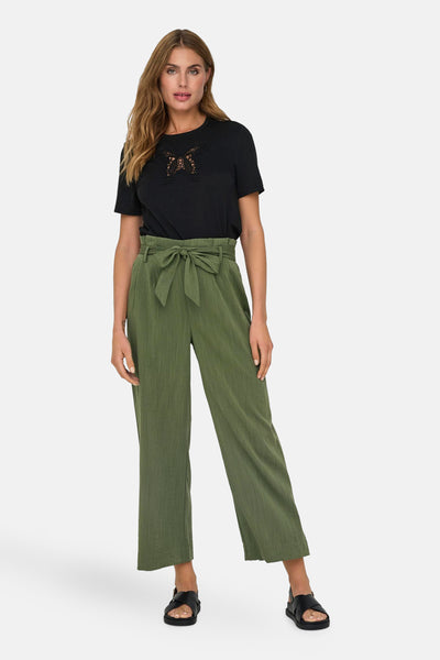 Pantalon chino 7/8 vert de ONLY®, porté avec une ceinture à nouer et un t-shirt noir à motif floral.
