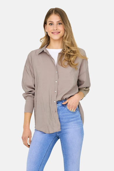 Beige langearmse chemise van ONLY, gedragen over een wit t-shirt en een blauwe broek.