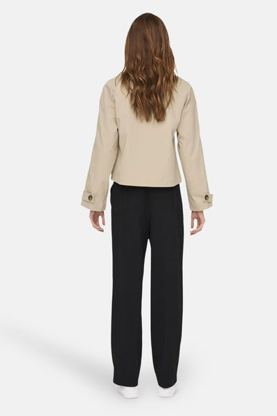 Veste courte beige par ONLY®, avec manches longues et détails de boutons, portée avec un pantalon noir.