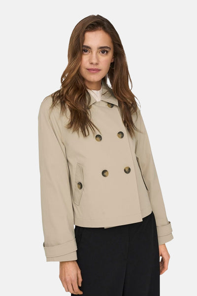 Veste courte beige by ONLY®, avec boutonnage croisé et poches discrètes, portée sur un pantalon noir.