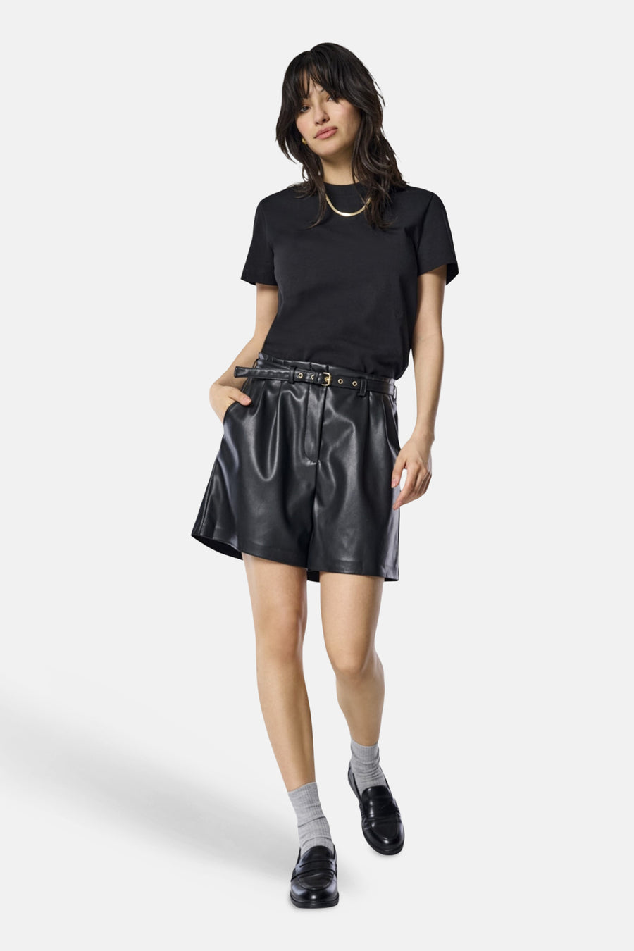 Korte imitatielederen short van ONLY®, gedragen met een zwart T-shirt en loafers met grijze sokken.