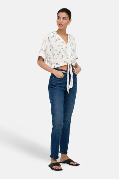 Chemise blanche à manches courtes de ONLY®, à motif floral bleu, nouée à la taille, portée avec un jean bleu et des sandales noires.