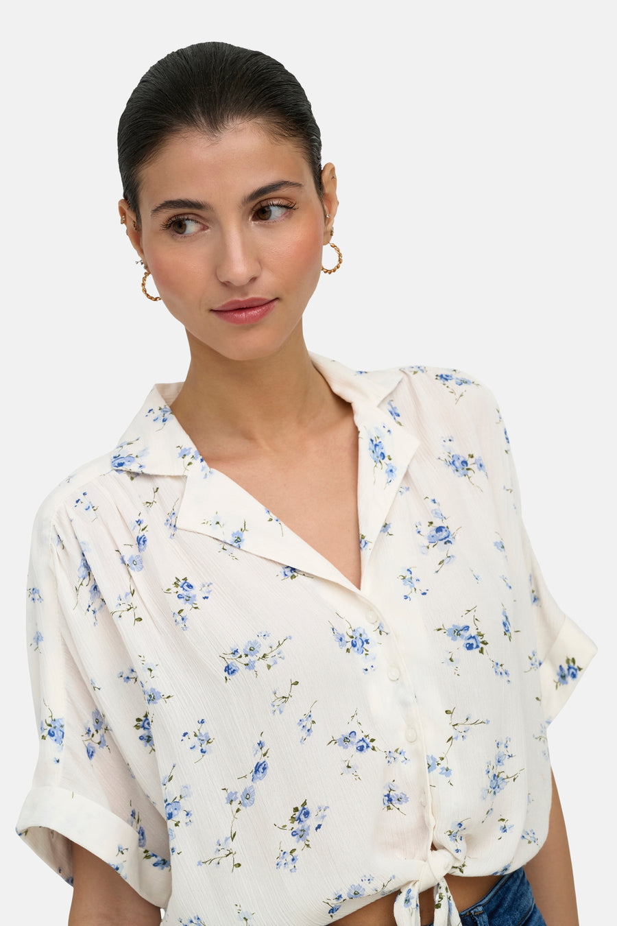 Wit overhemd met korte mouwen van ONLY® met blauw bloemenpatroon, geknoopt in de taille, gedragen door een vrouw met gouden oorbellen.