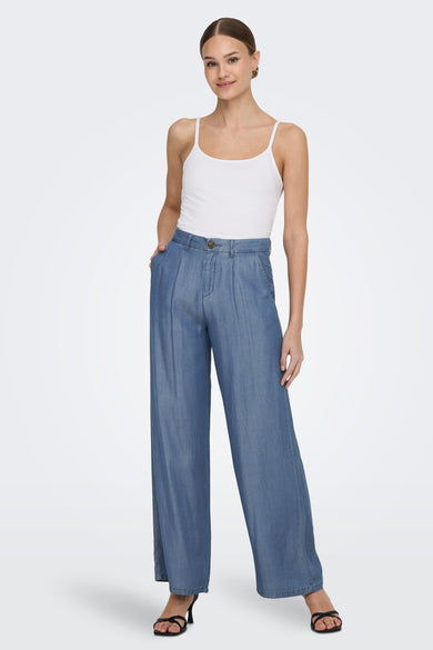 Pantalon en denim bleu moyen de JDY, style palazzo, porté avec un débardeur blanc et des sandales noires.