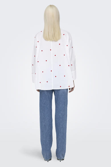 Chemise à manches longues blanche à motif de cœurs rouges par ONLY, portée avec un jean bleu.
