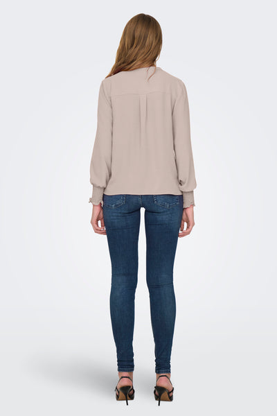 Lichtroze blouse van ONLY® met lange mouwen en smockmanchetten, gedragen met een spijkerbroek en hakken, van achteren gezien.