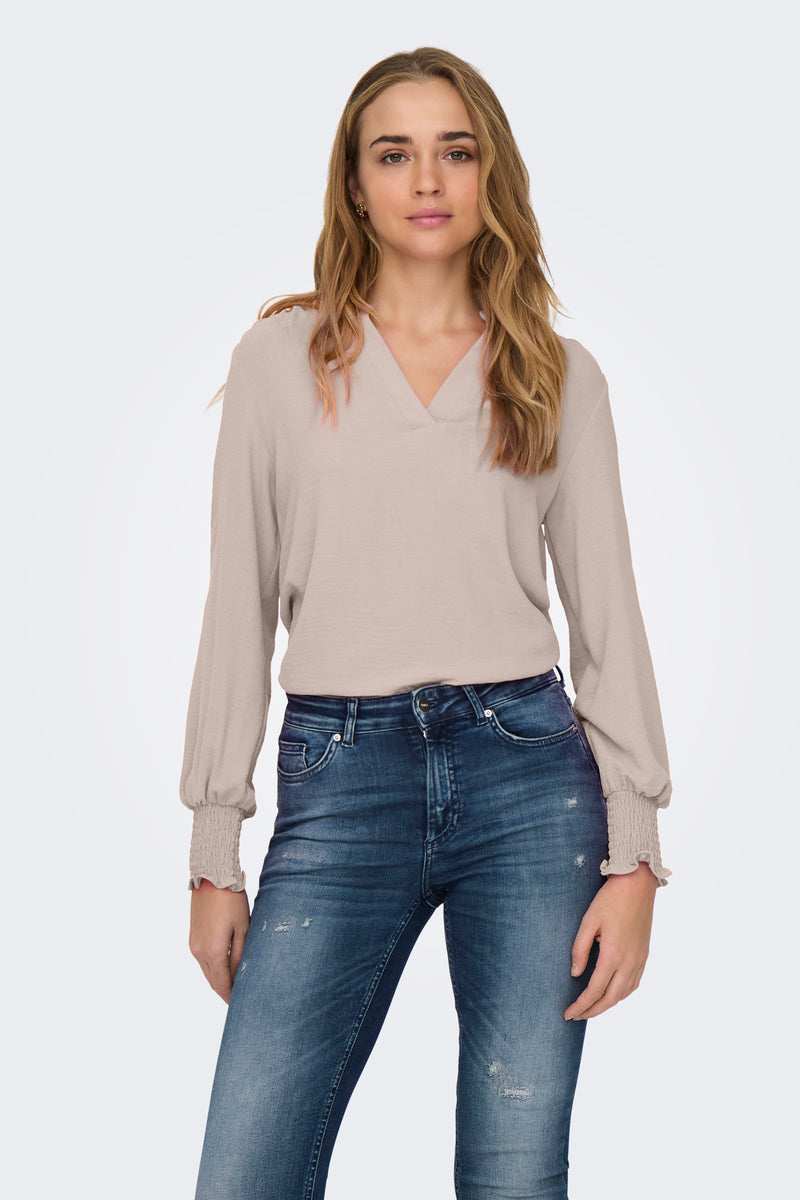 Roze blouse met lange mouwen van ONLY® met V-hals en smockmanchetten, gedragen met een blauwe jeans.