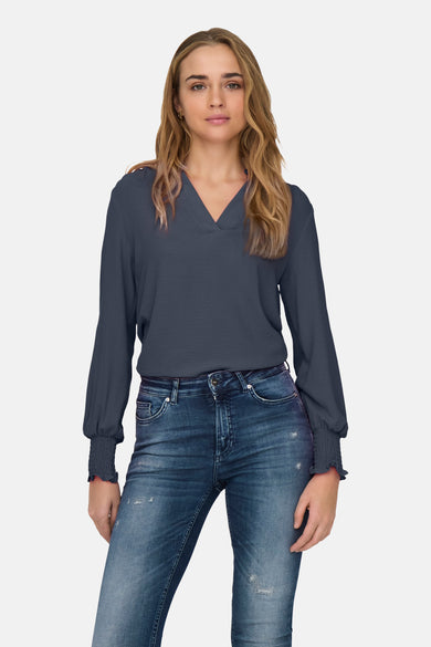 Blauwe blouse met lange mouwen van ONLY®, gedragen met een strakke blauwe jeans en zwarte hakken.