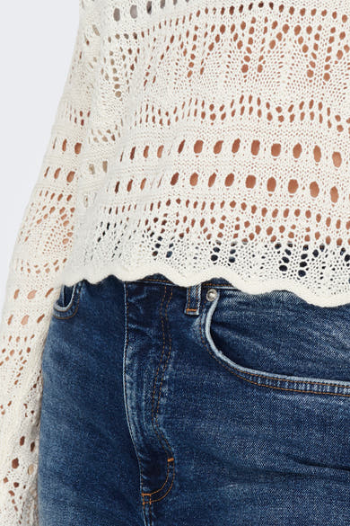 Pull à col rond blanc de JDY, avec motifs ajourés sur tricot texturé, porté avec un jean taille haute bleu.
