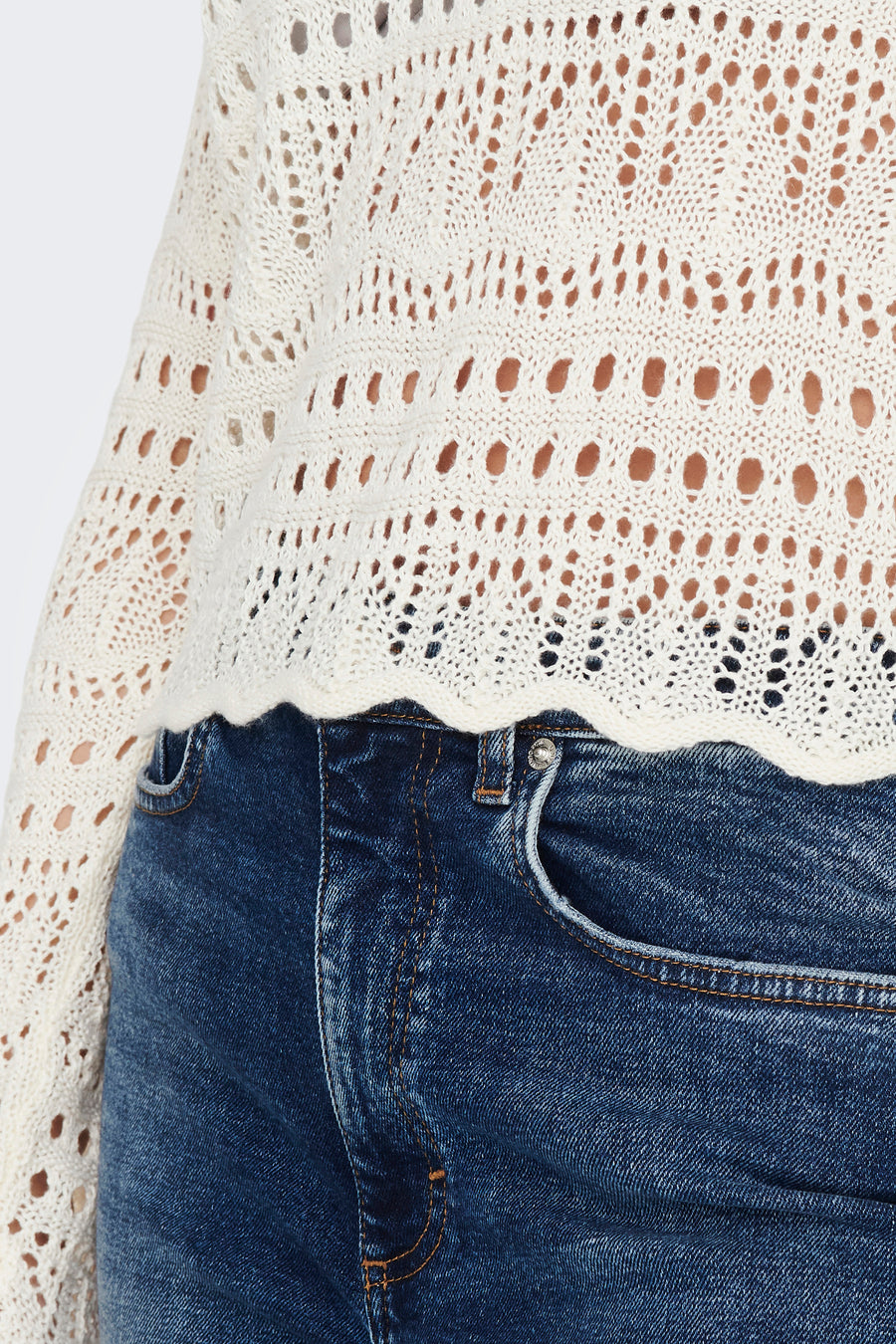 Pull à col rond blanc de JDY, avec motifs ajourés sur tricot texturé, porté avec un jean taille haute bleu.
